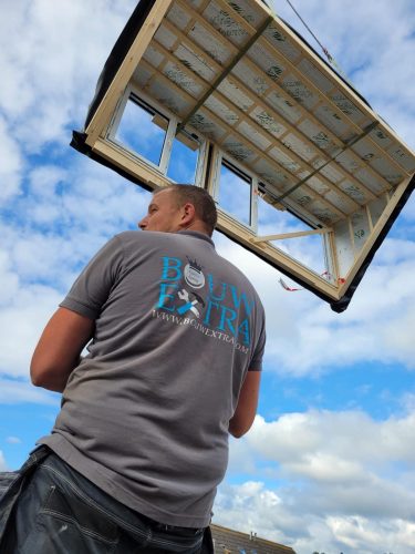 Een medewerker van Bouwextra kijkt omhoog terwijl een prefab dakconstructie met een kraan wordt geplaatst op een bouwlocatie.